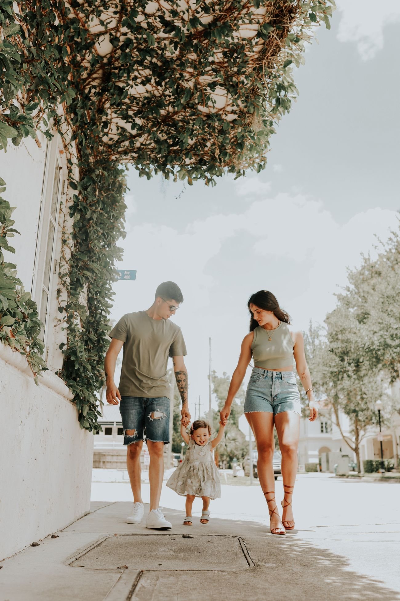 Familia joven paseando de la mano con su hija pequeña por una calle soleada
